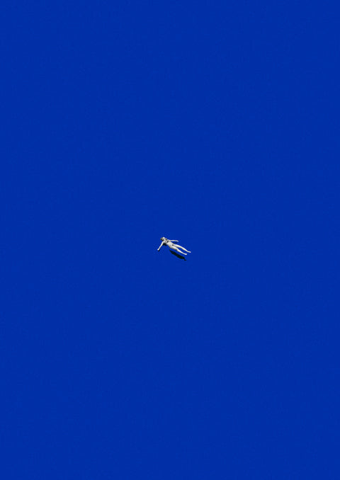 A tiny figure in white floating against a vast, solid blue background.